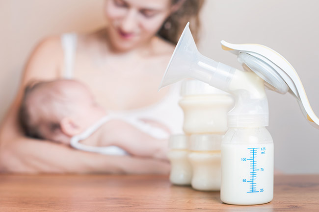 An image of a mother and her baby with a breast pump in the foreground